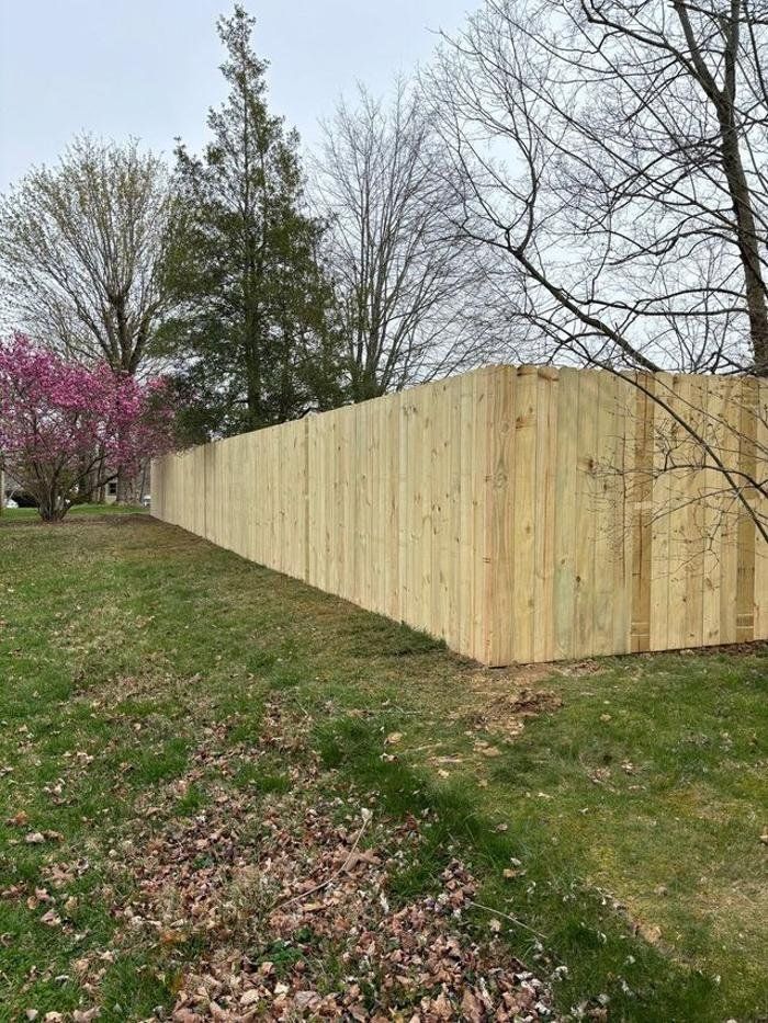 A long wooden fence surrounds a grassy field with trees in the background.