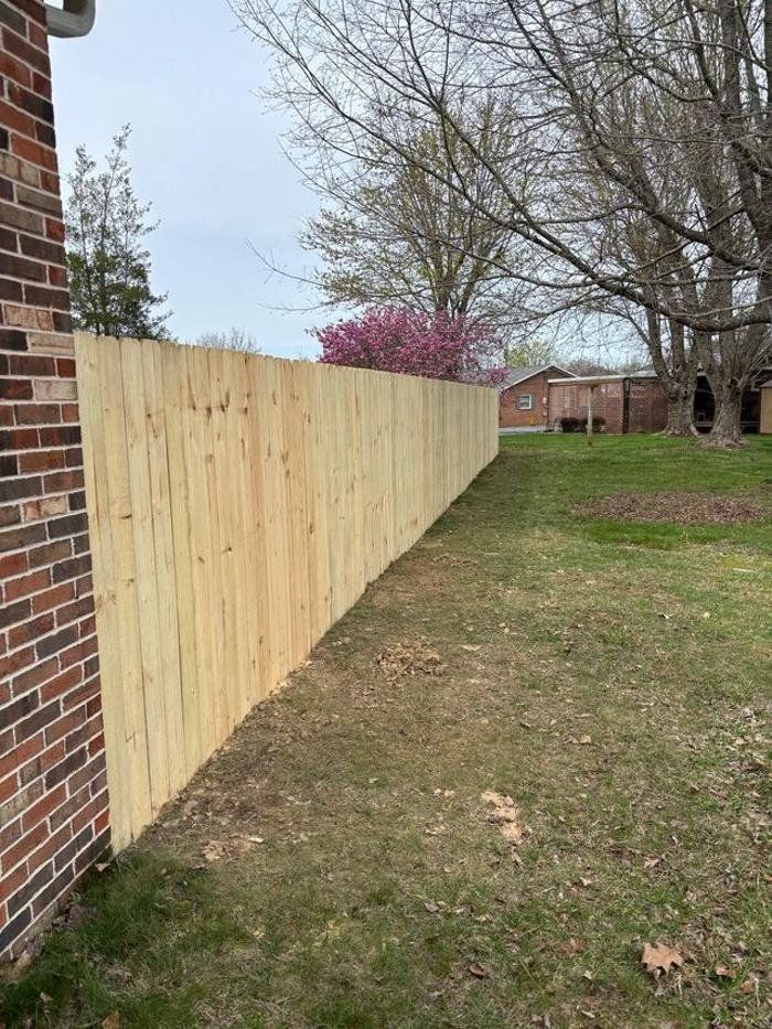 A wooden fence is sitting next to a brick wall in a yard.