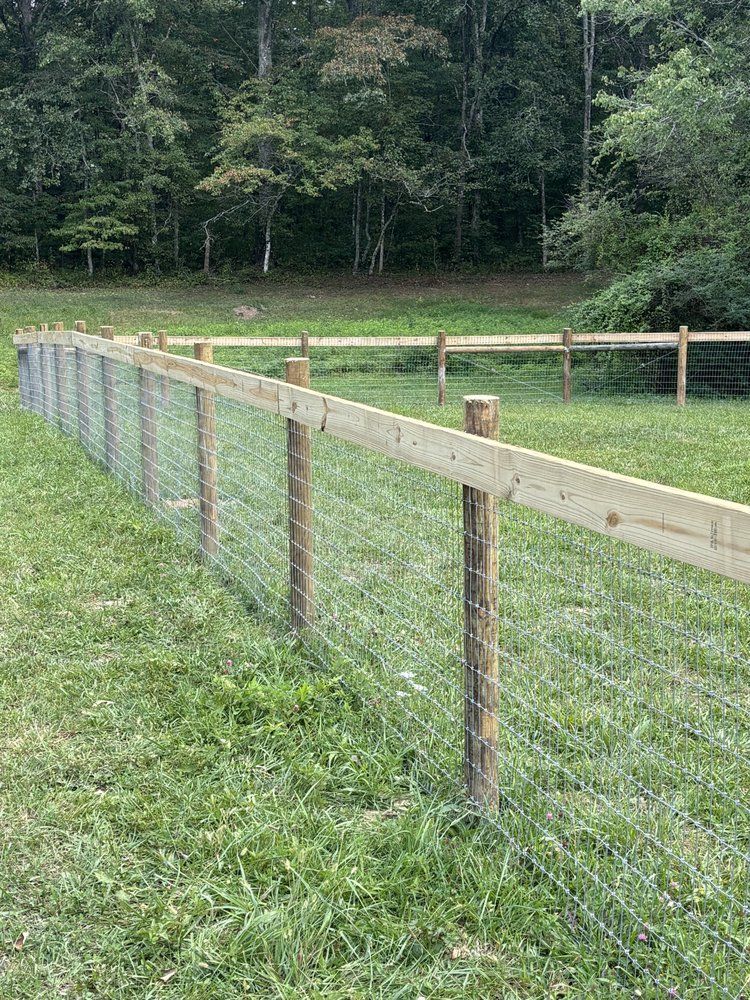 A wooden fence with barbed wire surrounding a grassy field.