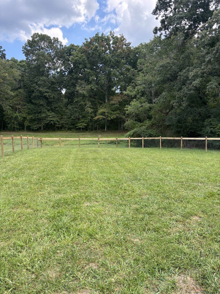 A large grassy field with a wooden fence and trees in the background.