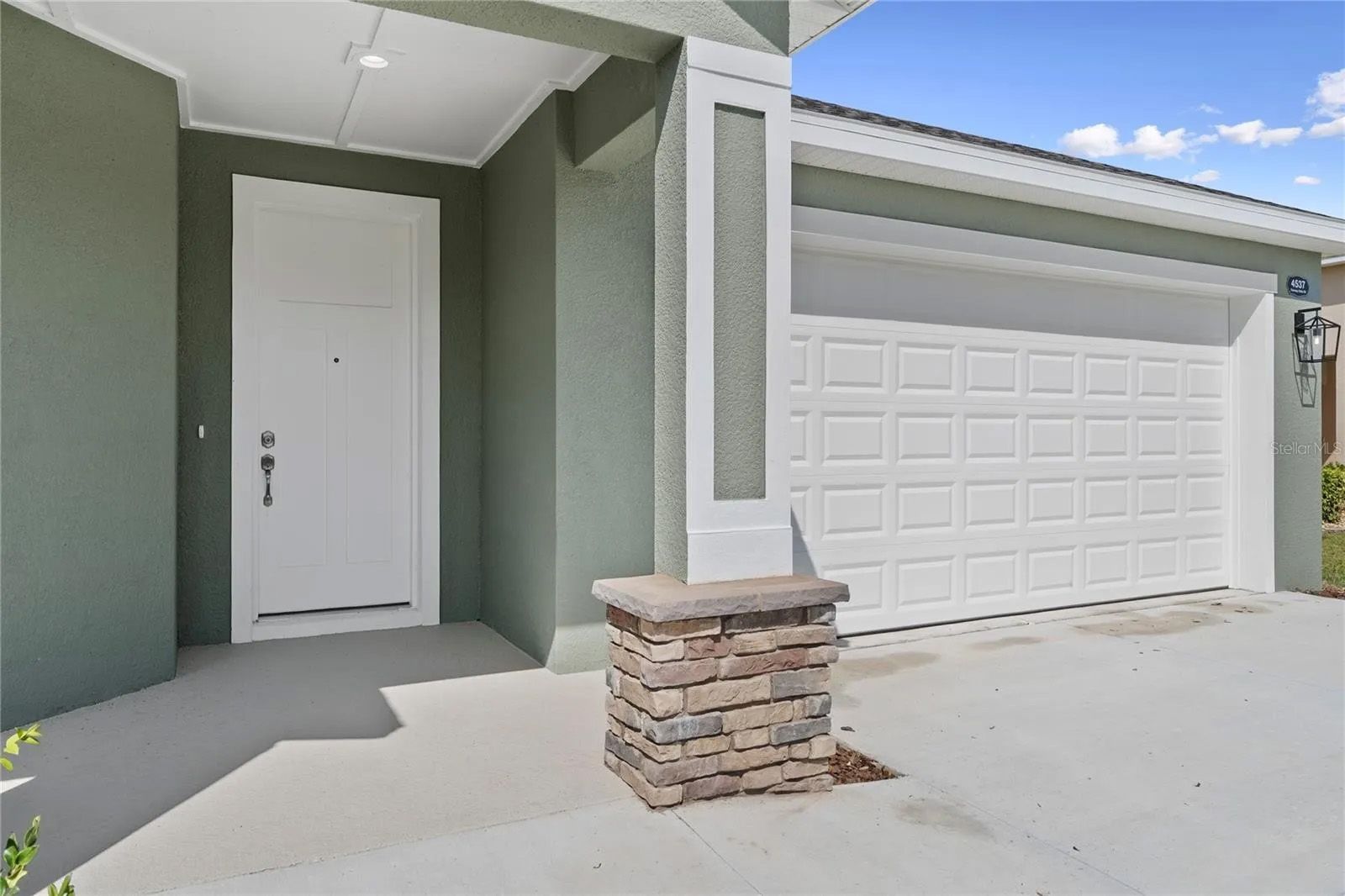 A house with a white garage door and a stone pillar in front of it.