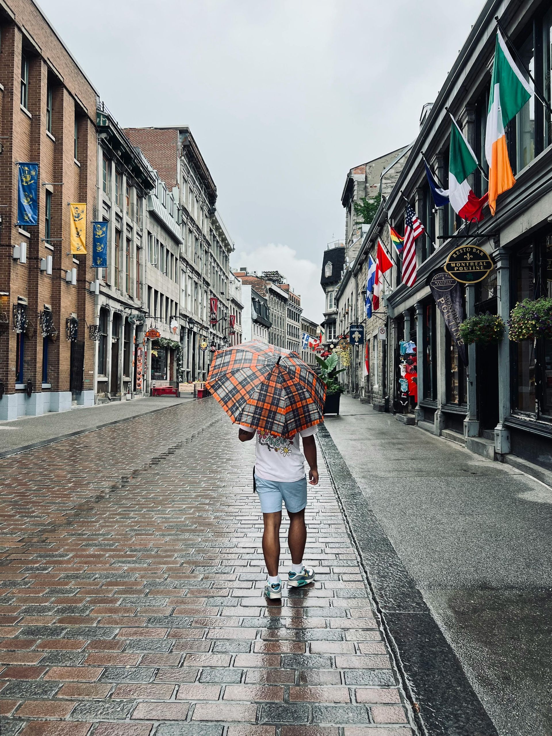 A man is walking down a cobblestone street with an umbrella in the rain.