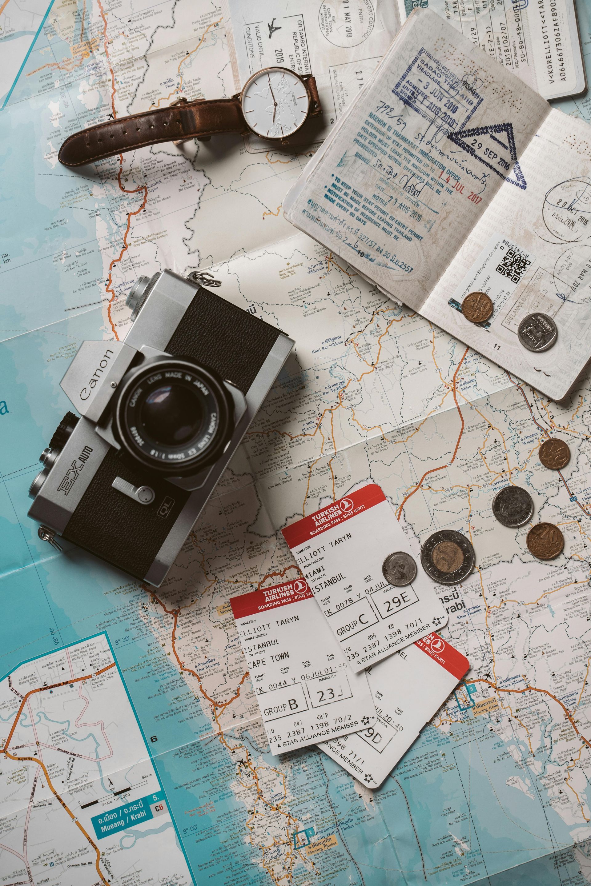 A camera , watch , passport , tickets and coins are on a map.