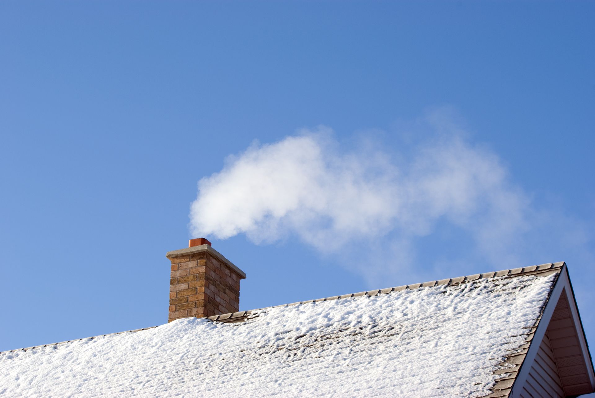 Smoke is coming out of a chimney on a snowy roof