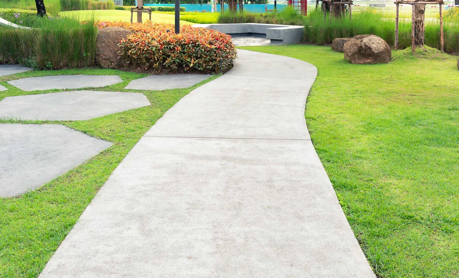 Stone pathway winding through green grass and garden beds.