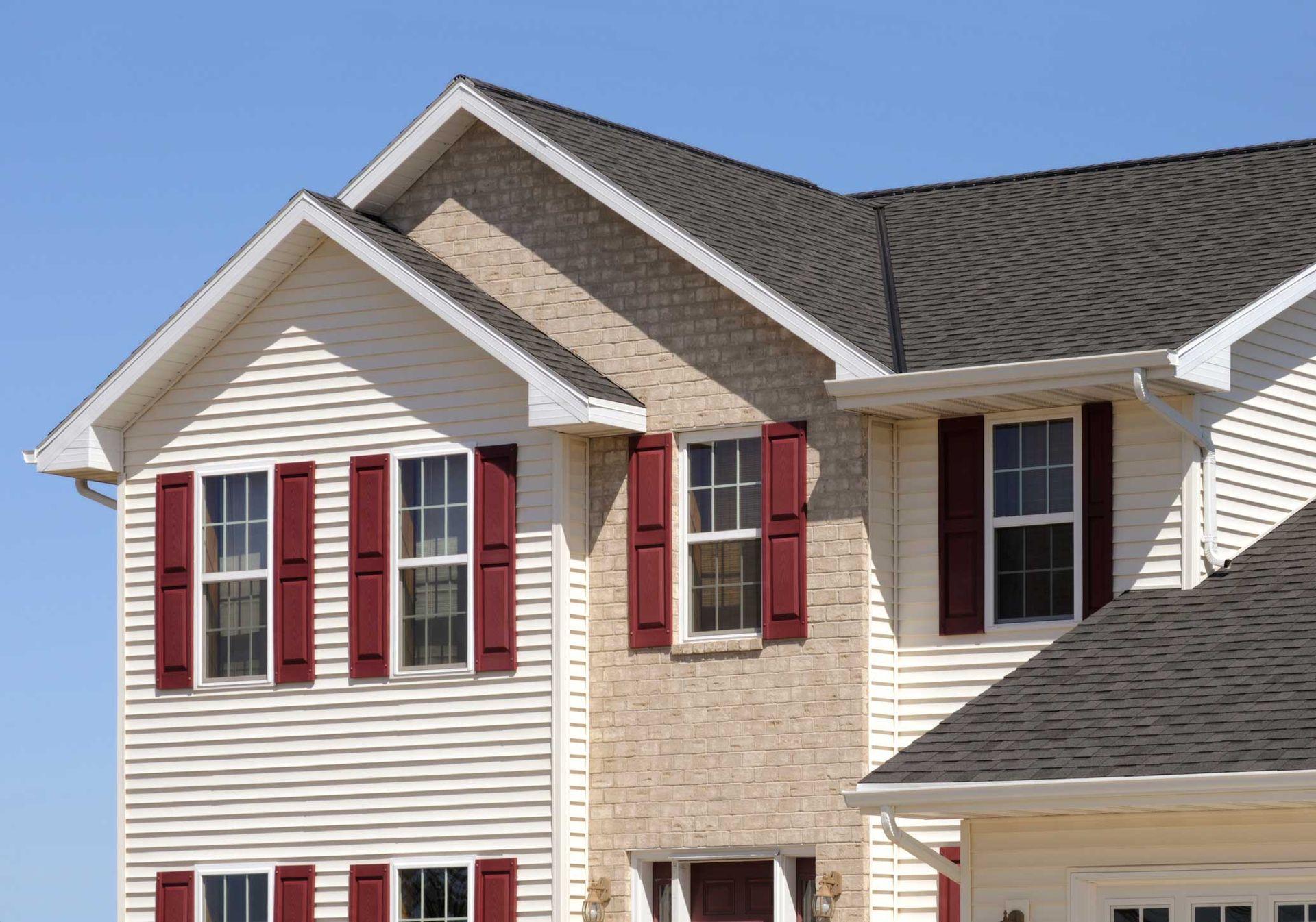 Two-story house with tan siding and red shutters.