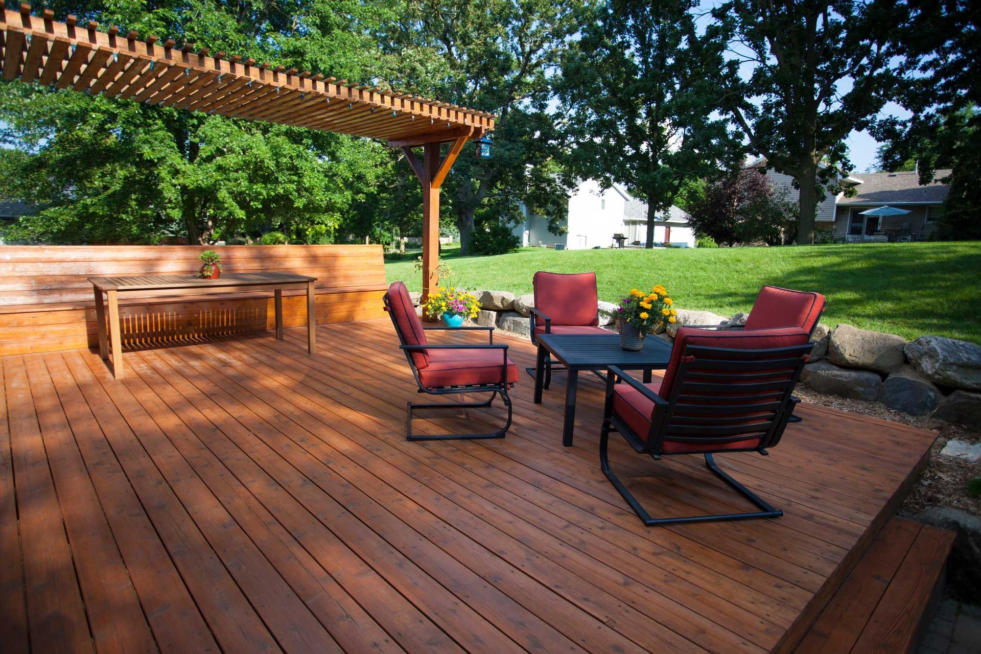 Wooden deck with outdoor furniture, pergola, and lush green backyard.