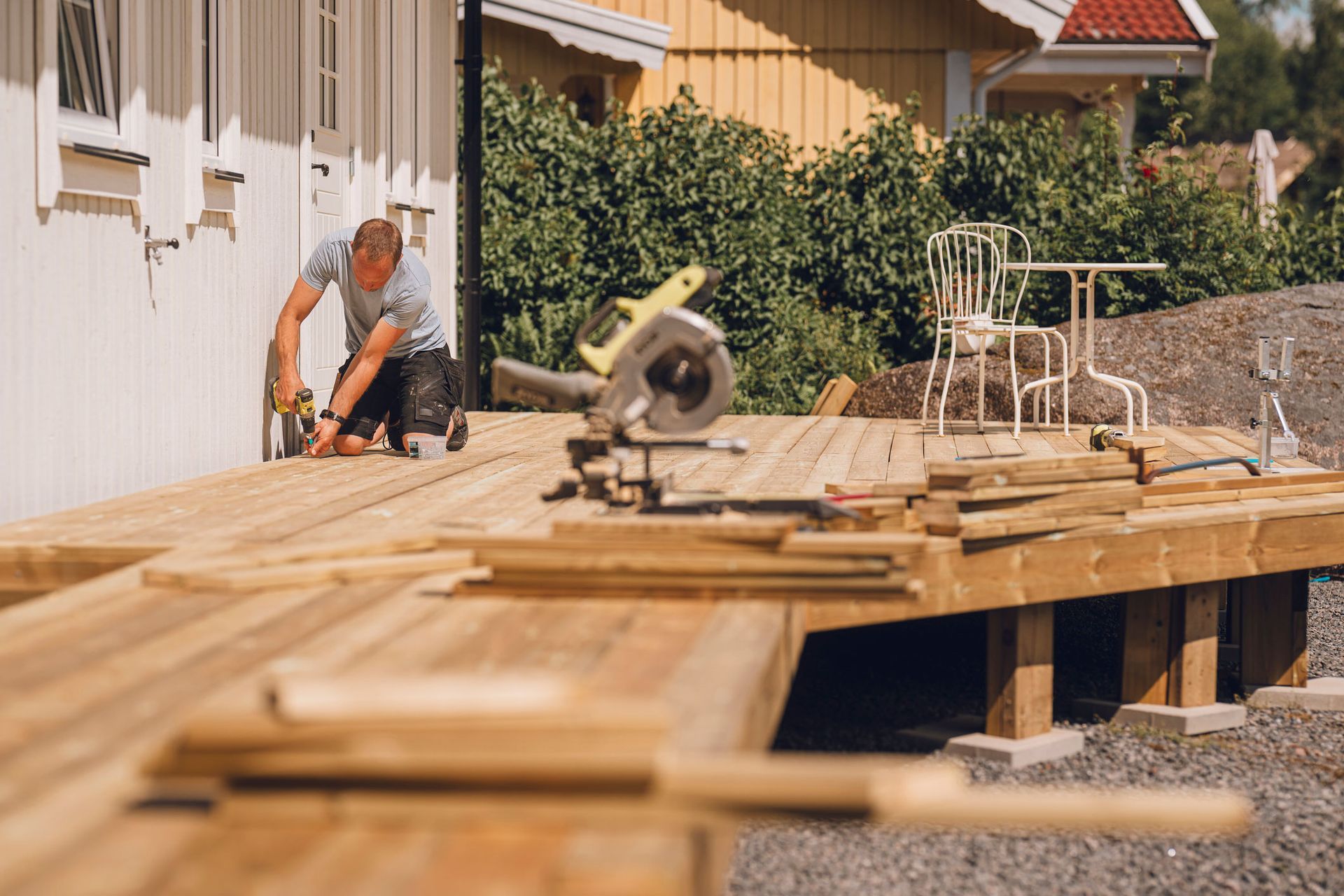 Man kneeling, using a drill on a wooden deck.
