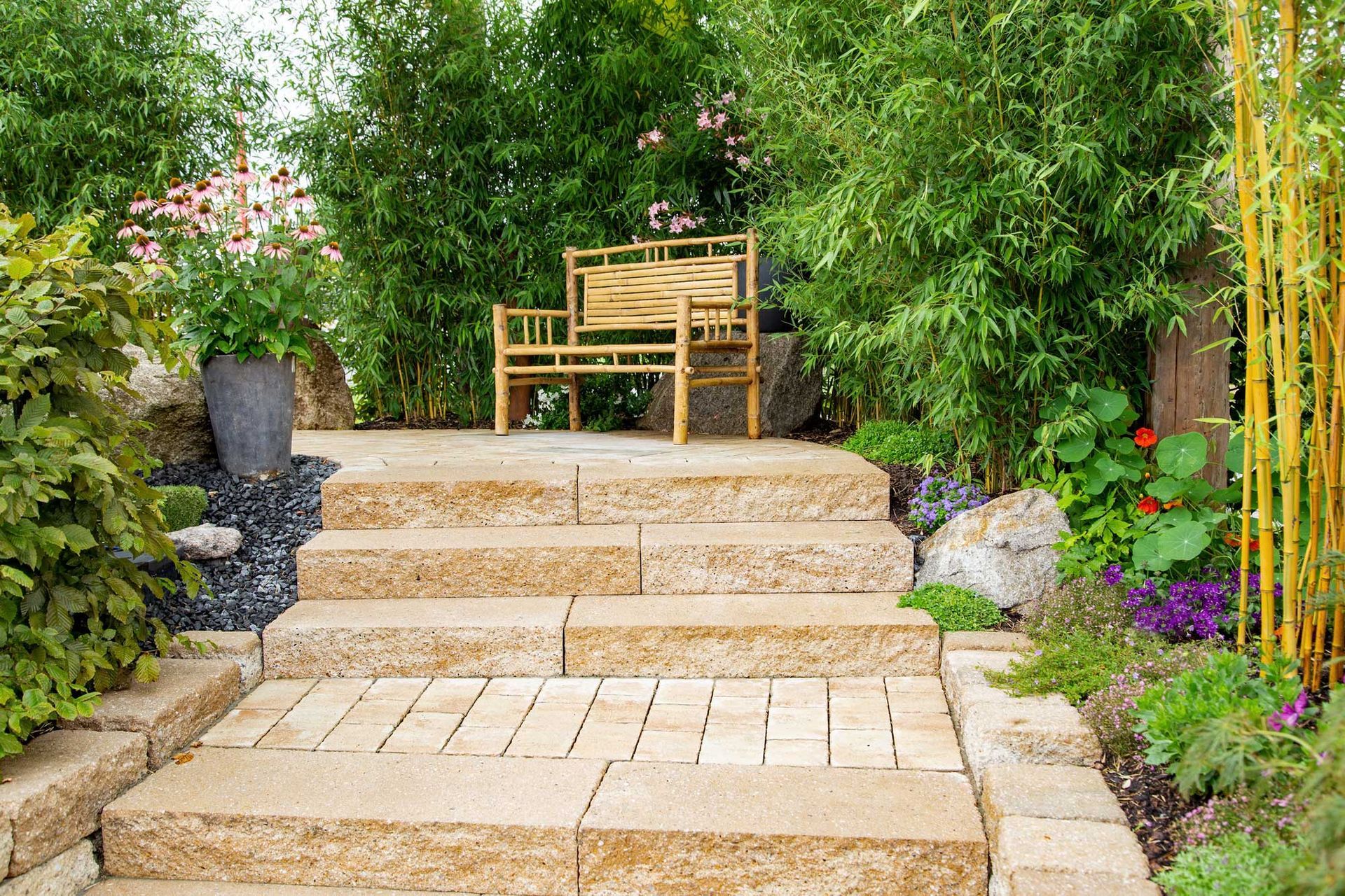 Stone steps lead to a bamboo bench in a lush garden.