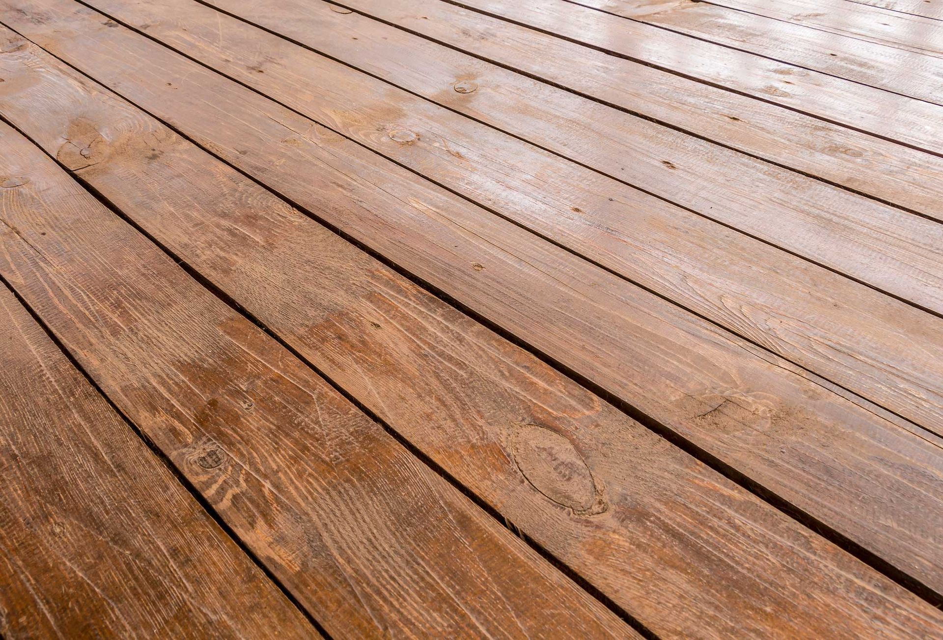 Wooden deck planks, brown with visible grain and gaps, angled perspective, sunlight.