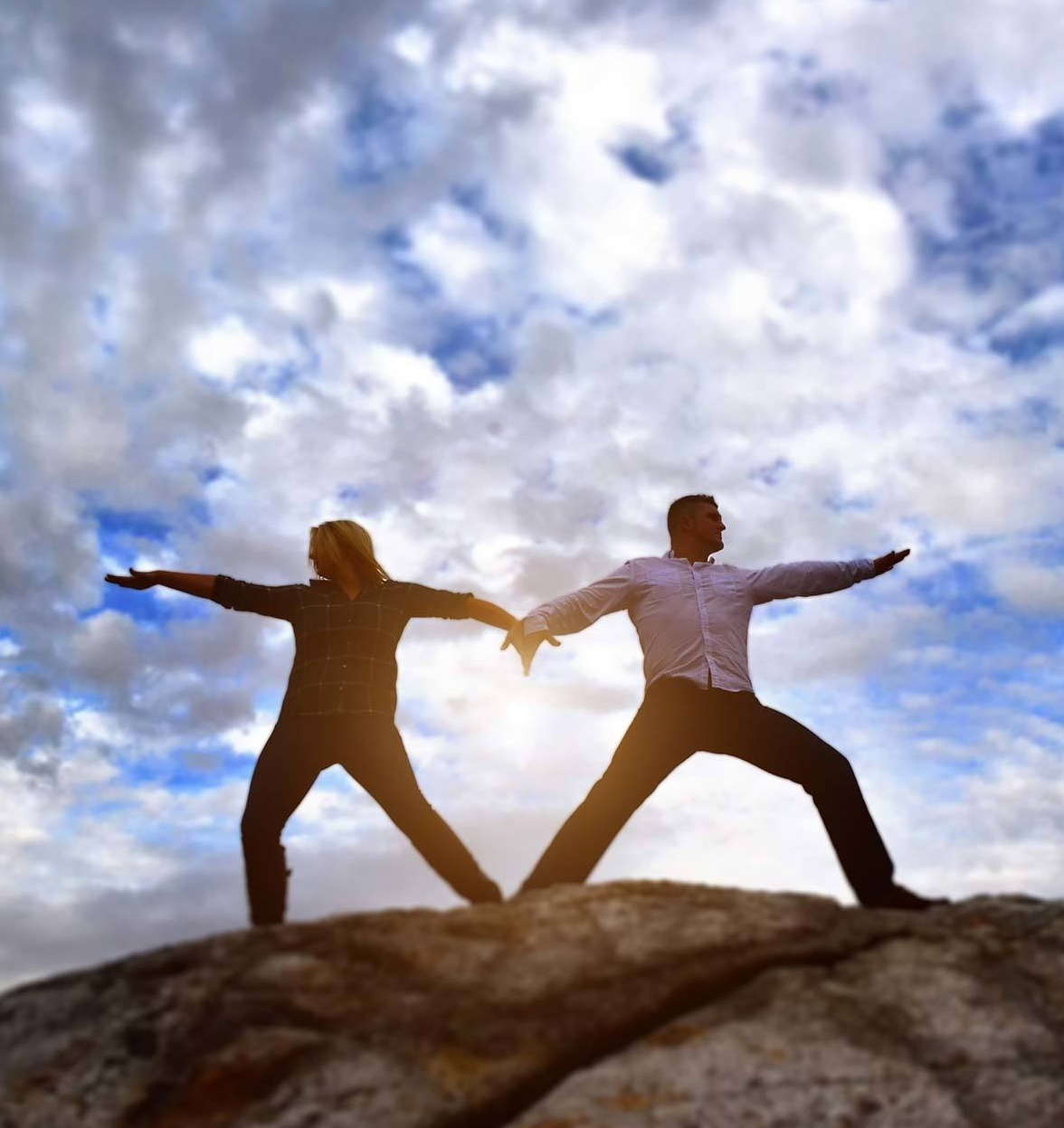 An engagement photo of man and a woman are standing on a rock doing a yoga pose by Rogers Photography.