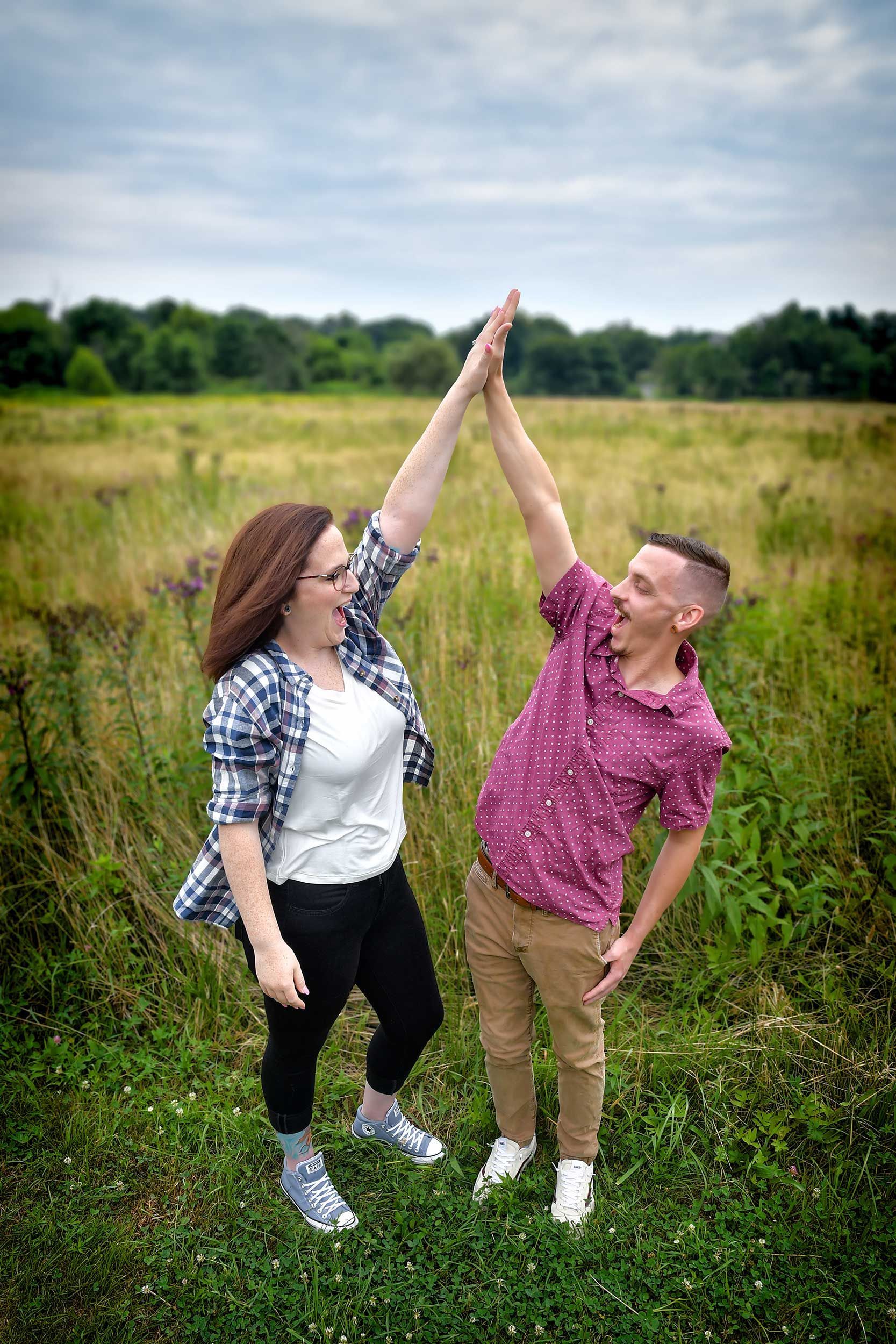 Engagement photograph of a couple giving each other a high five in a field by Rogers Photography.