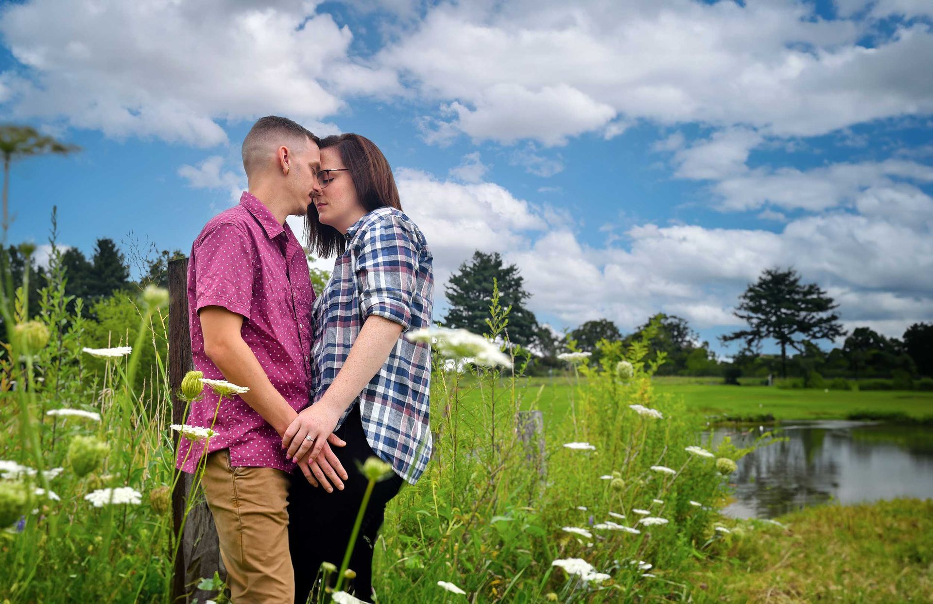 An engagement photo of man and a woman standing in a field holding hands by Rogers Photography.