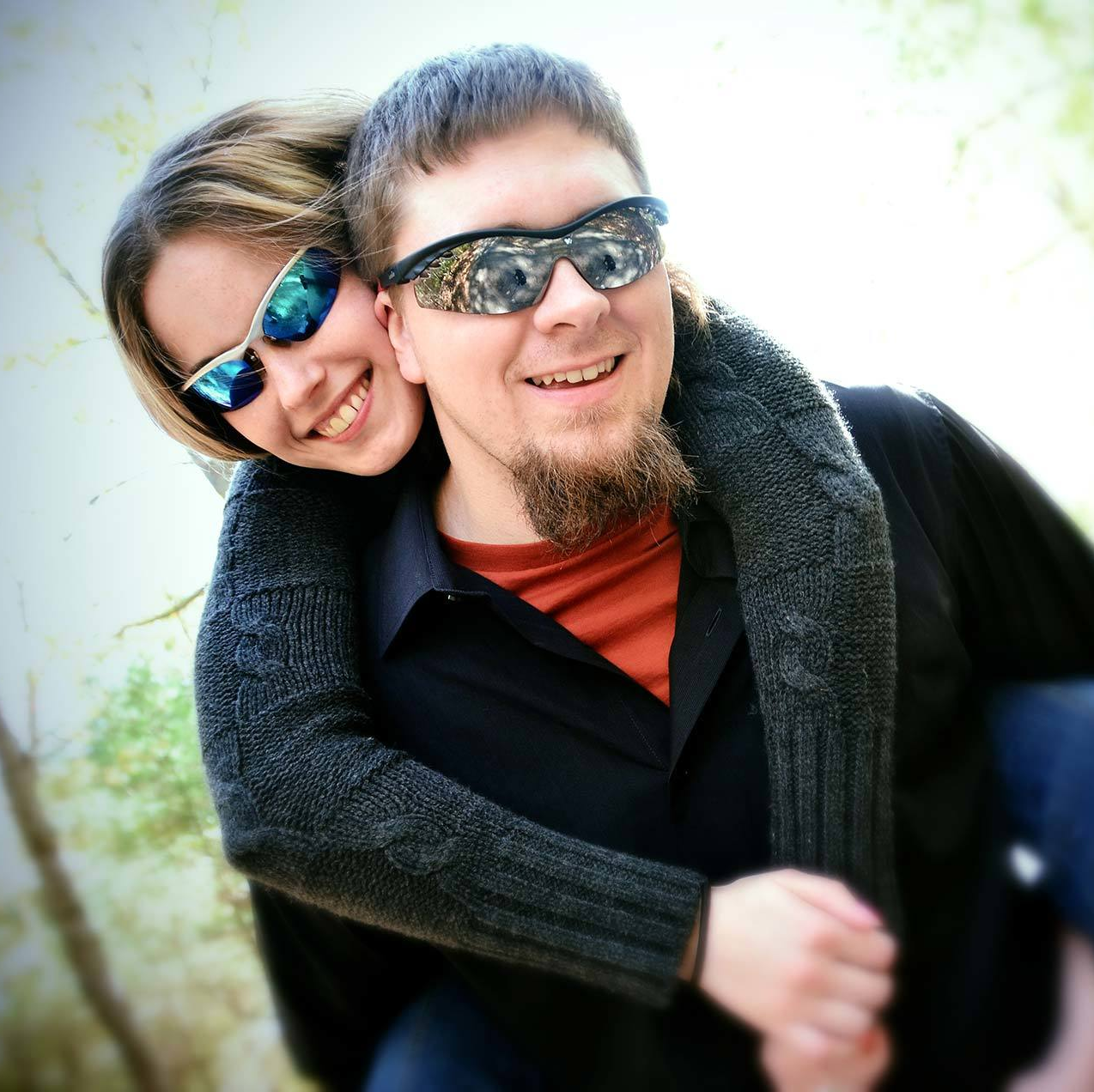 An engagement photograph of a man carrying a woman on his back wearing sunglasses by Rogers Photography