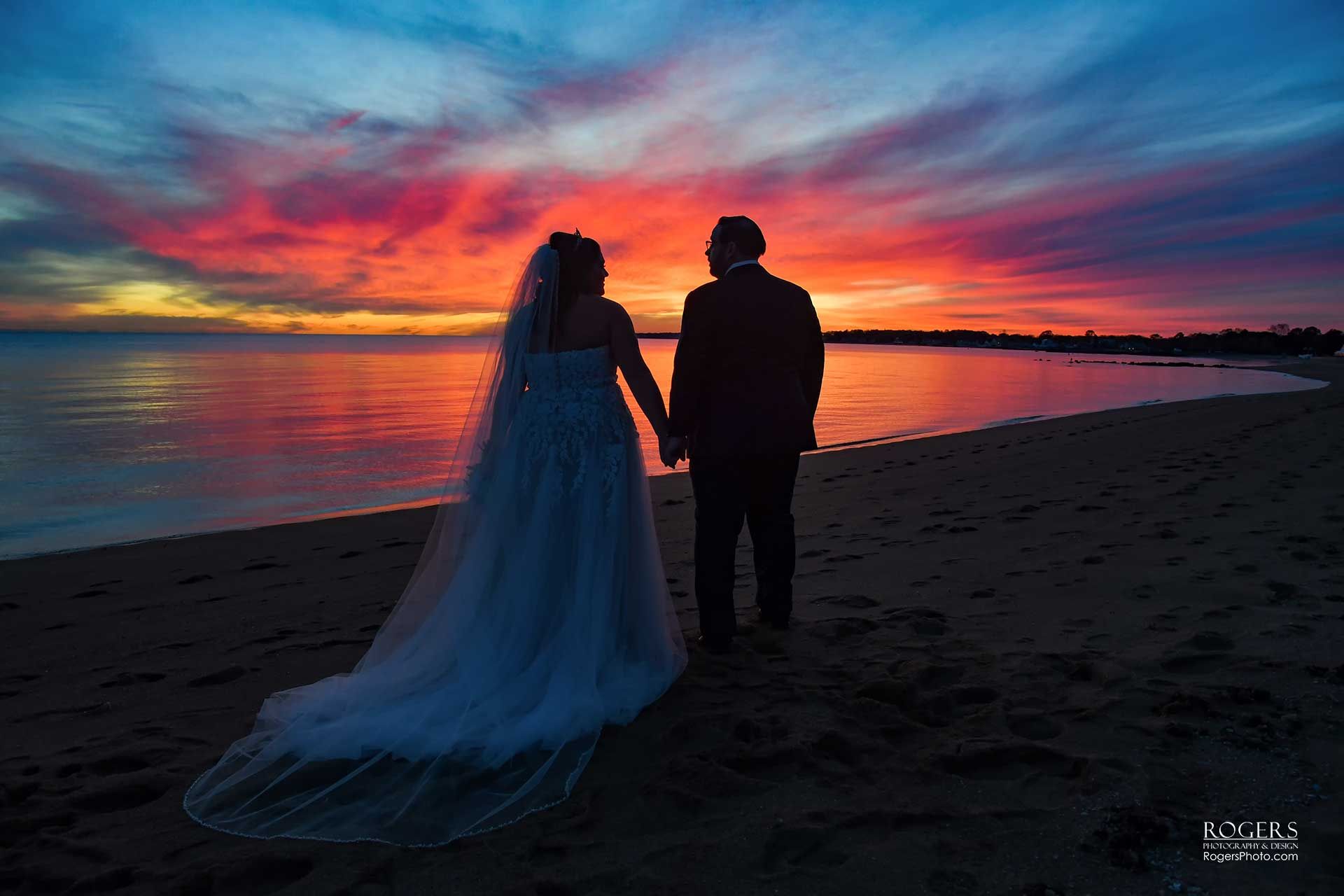 A bride and groom holding hands on the beach at sunset