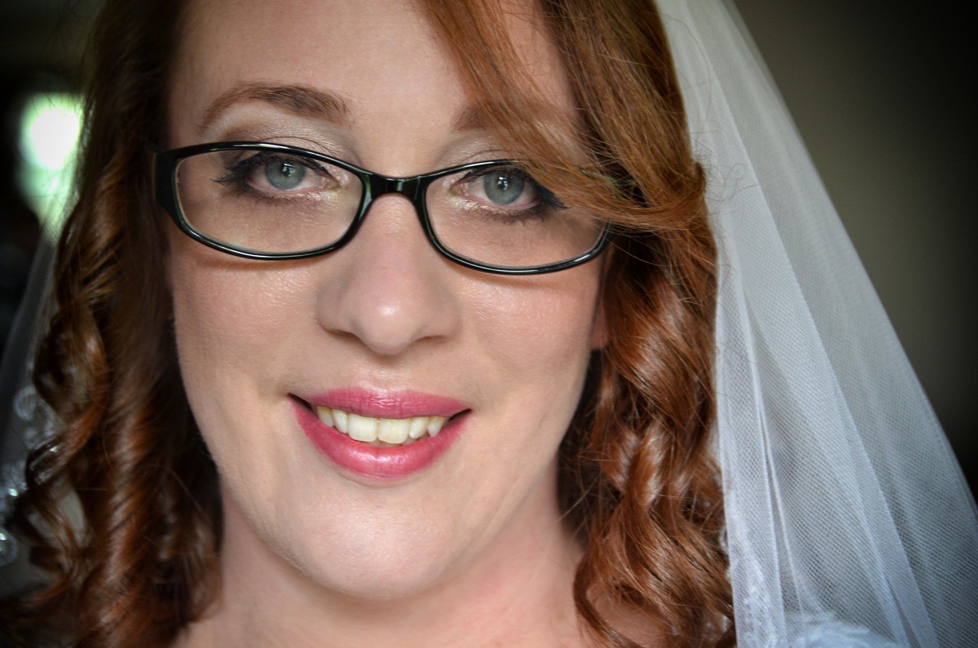 a bride wearing glasses and a white veil smiles for the camera after major photo retouching