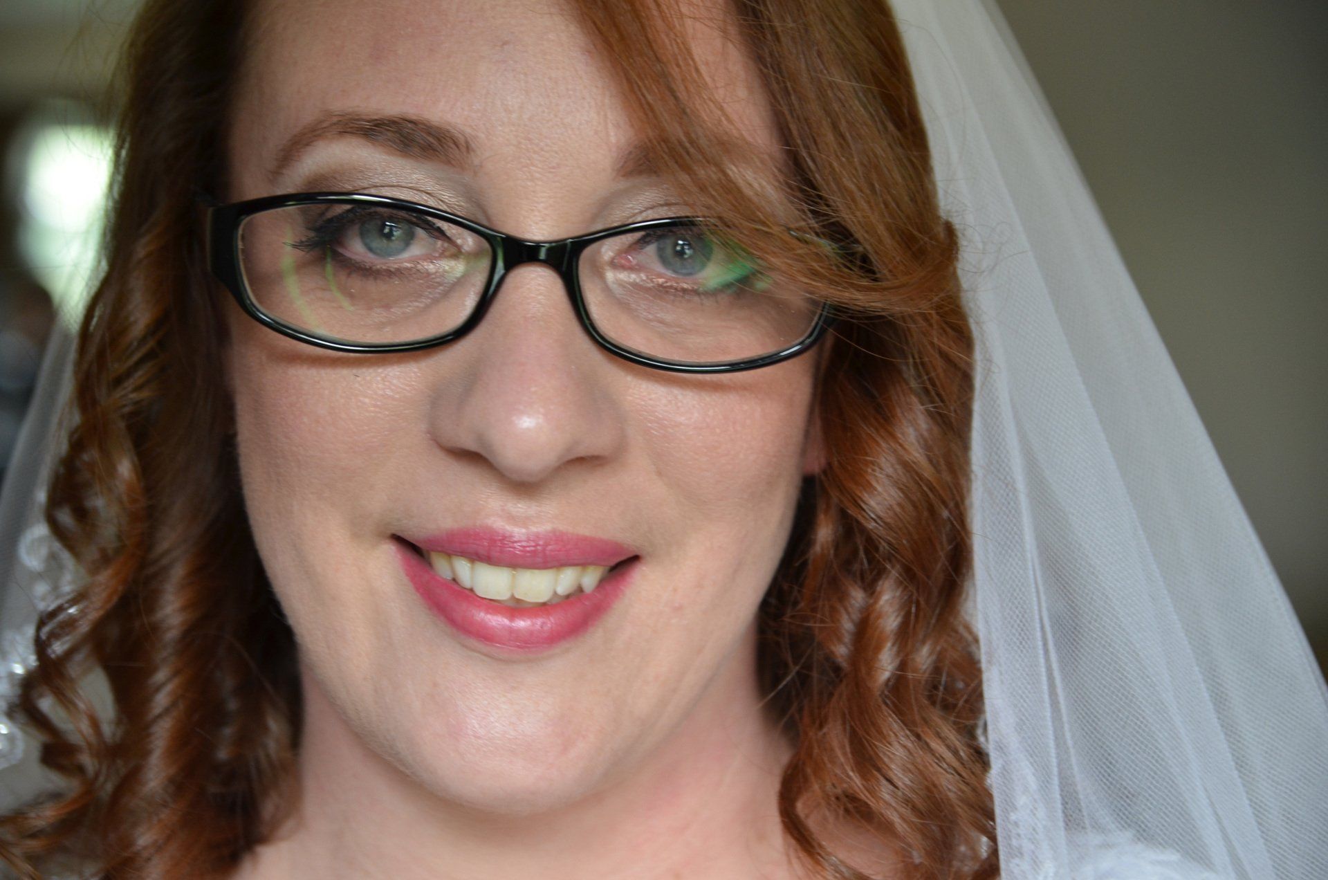 a bride wearing glasses and a white veil smiles for the camera before major photo retouching