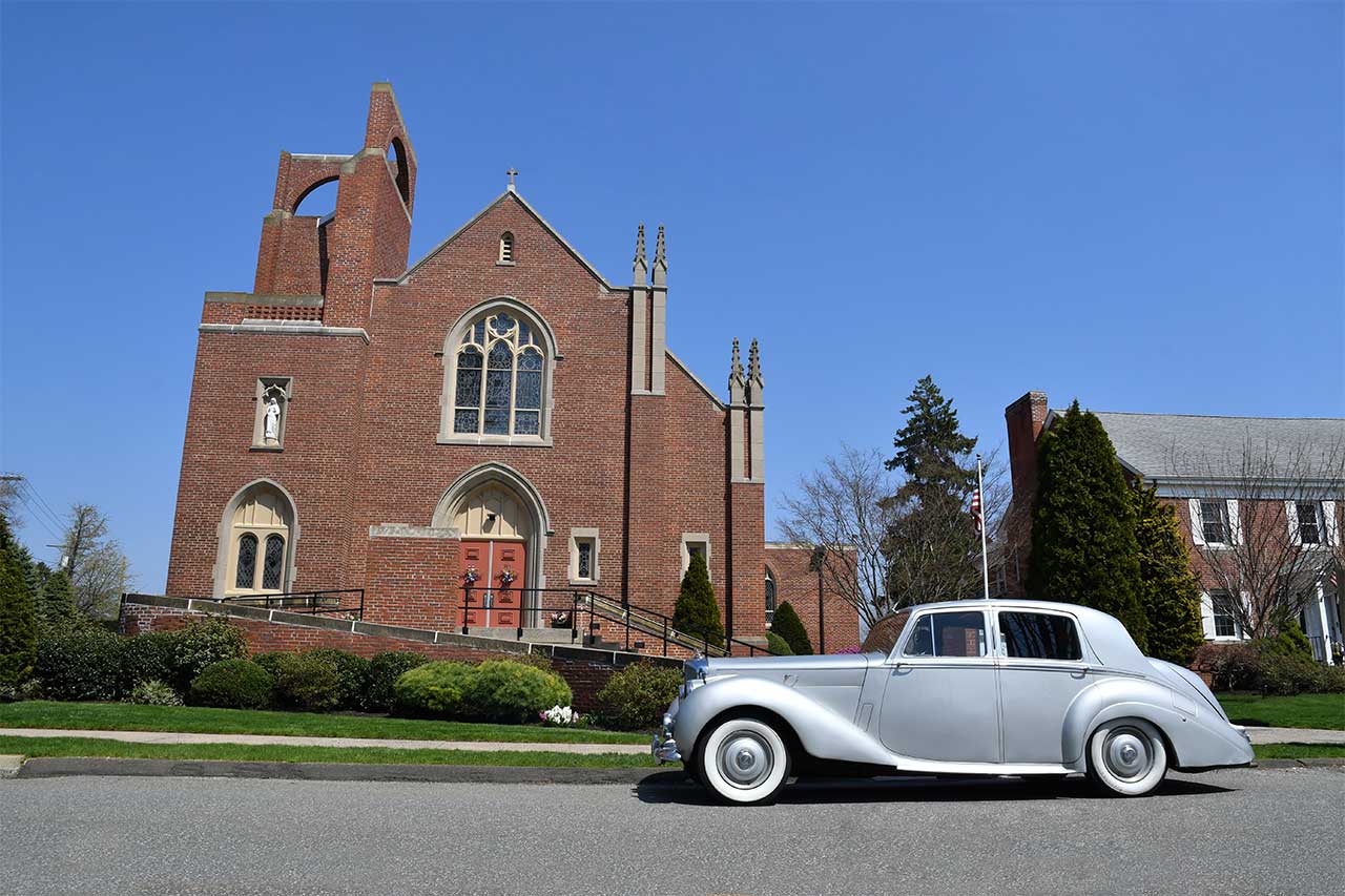 a silver Rolls Royce car is parked in front of a church after photo retouching