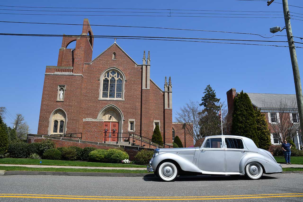 a silver Rolls Royce car is parked in front of a church before photo retouching