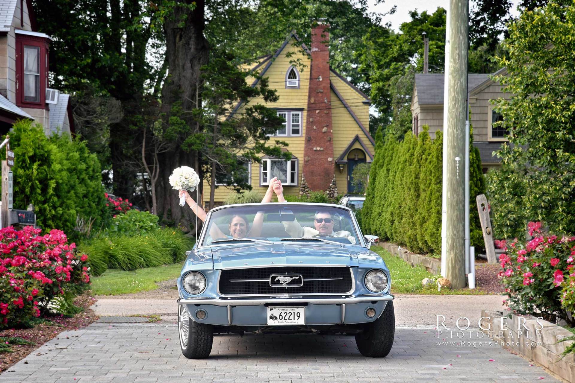 A bride and father are driving down a street in a mustang to her wedding ceremony at Madison Beach Hotel wedding photographed by Rogers Photography in Connecticut.