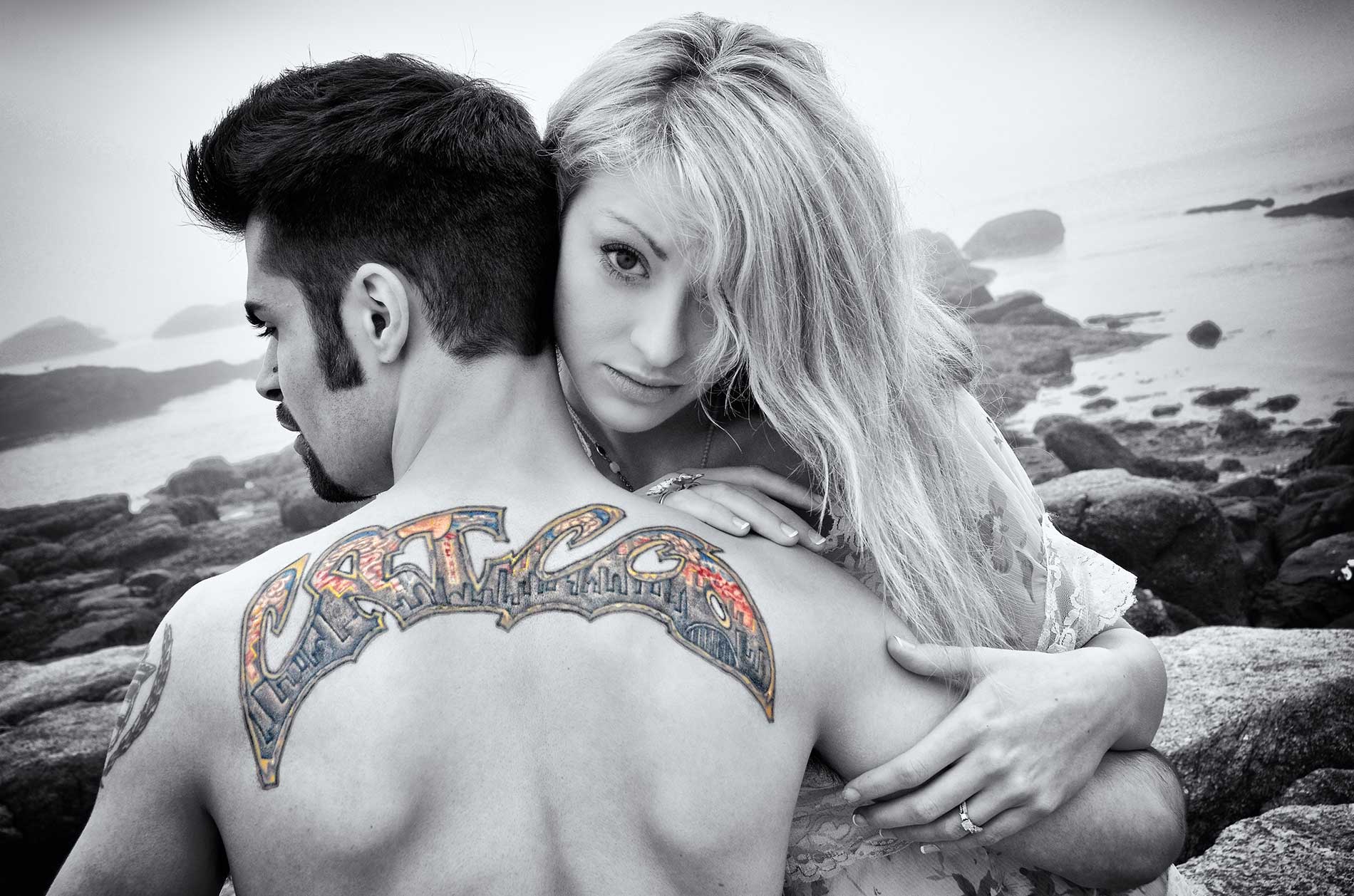 An engagement portrait of a man with a tattoo on his back is being hugged by a woman by Rogers Photography.