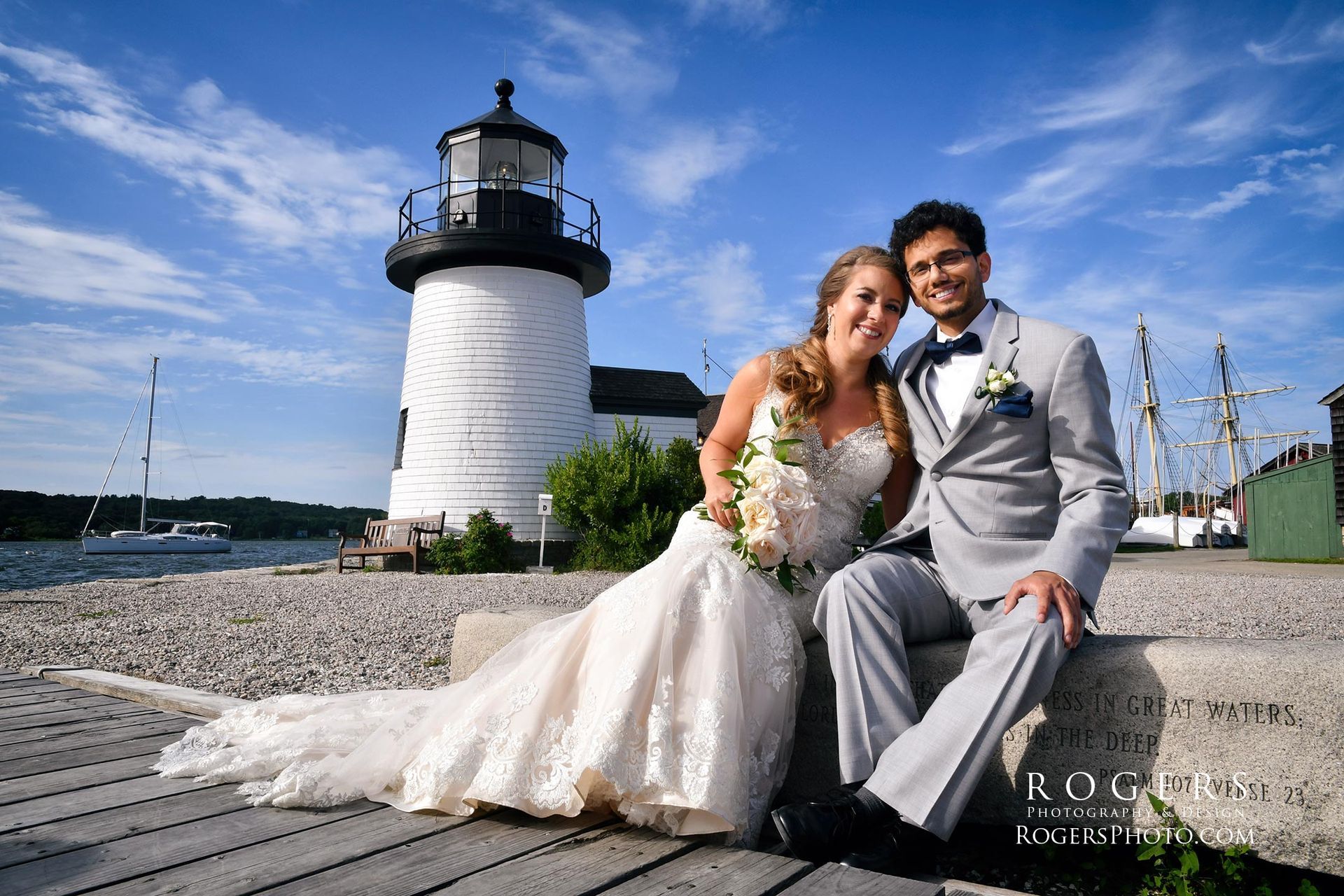 A bride and groom pose in front of a lighthouse at Mystic Seaport  wedding photographed by Rogers Photography in Connecticut.
