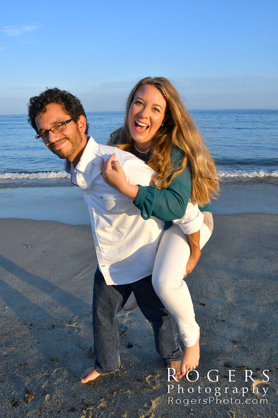 An engagement photo of man is giving a woman a piggyback ride on a Connecticut Beach in Niantic CT by Rogers Photography.