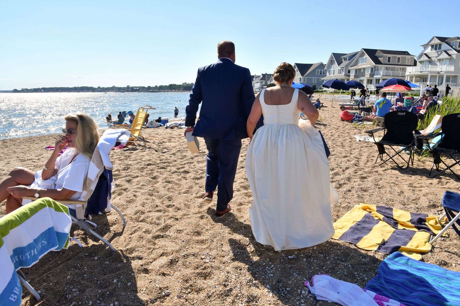 a bride and groom are walking on a beach full of people before major photo retouching