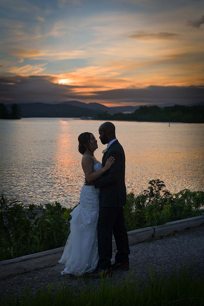 a bride and groom are dancing in front of a lake at sunset after major photo retouching