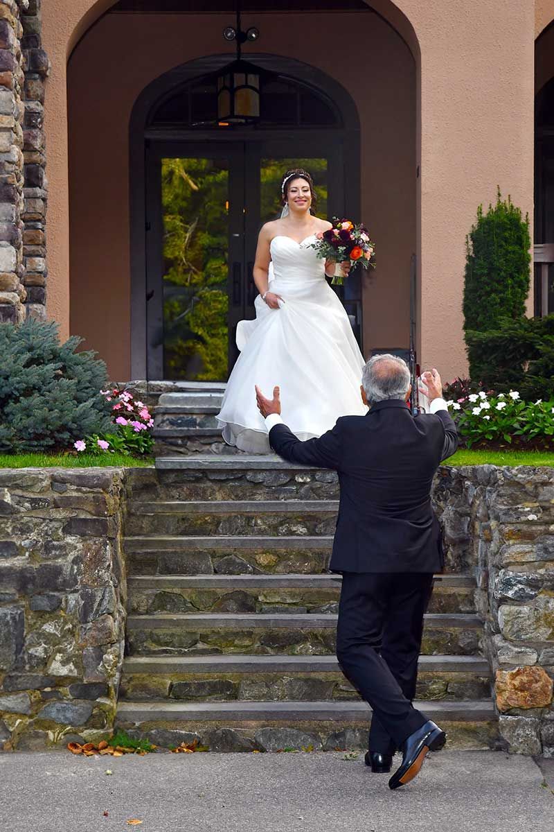 a bride is walking down a set of stairs to meet her father after major photo retouching