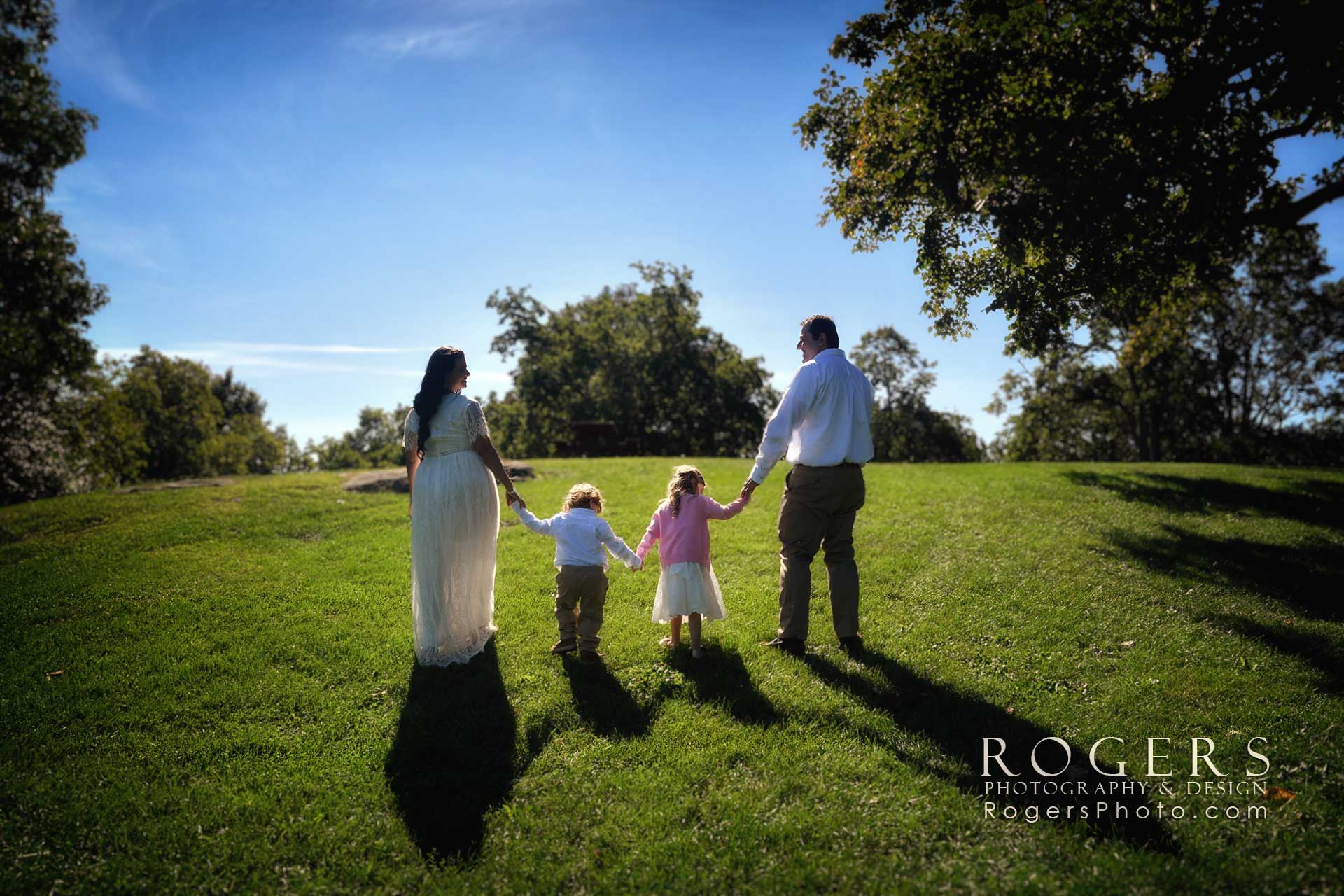 A portrait of family holding hands in a grassy field by the beach at Chaffinch Island in Guilford by Rogers Photography.