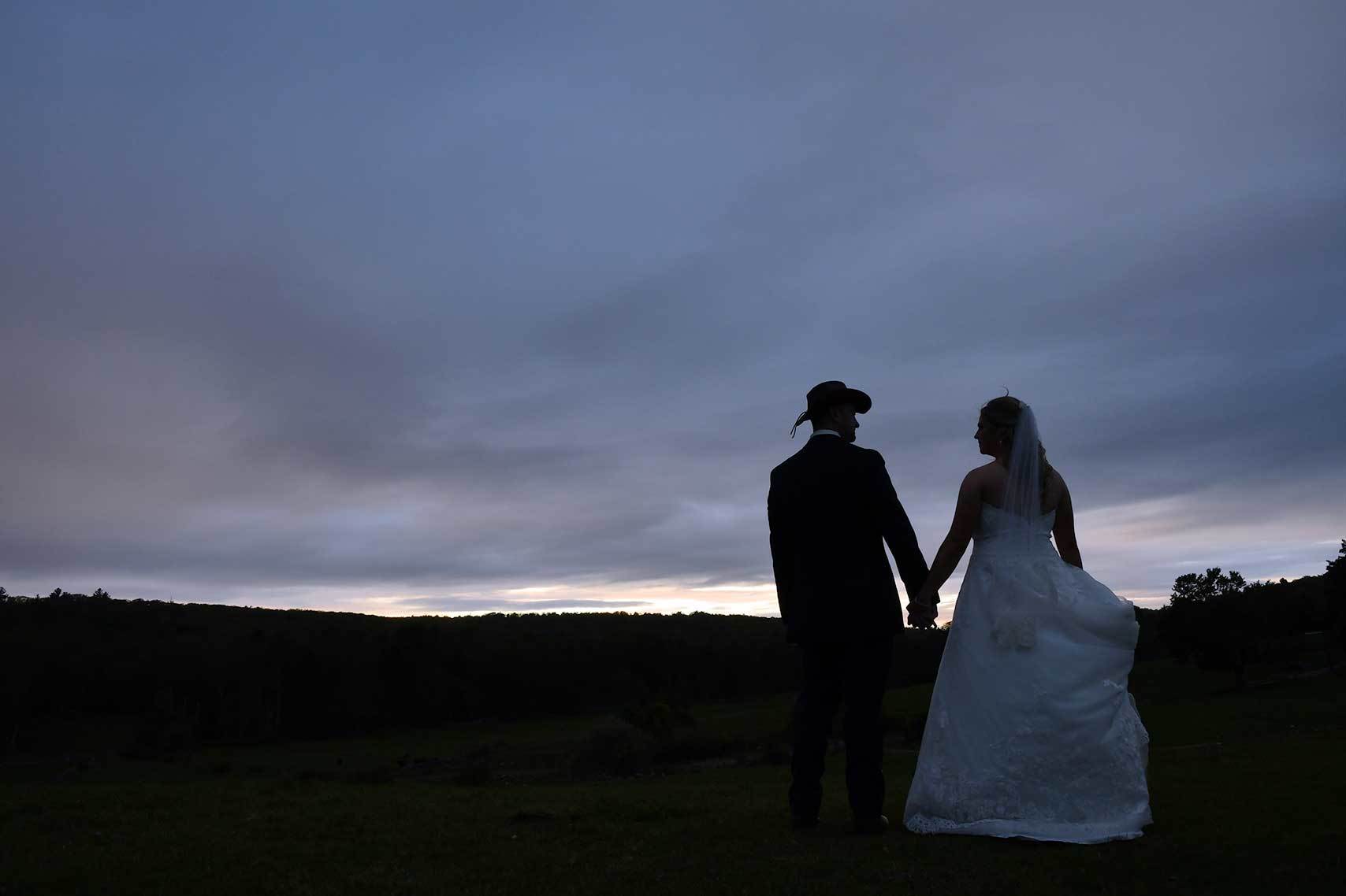 a bride and groom standing in a field holding hands at sunset before photo retouching