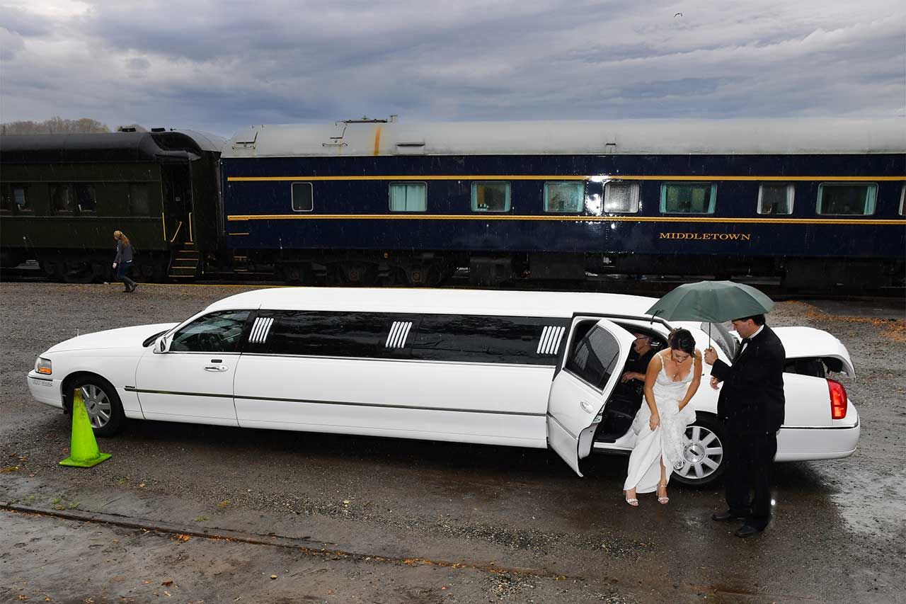 a bride exiting a white limousine is parked in front of a train before major photo retouching