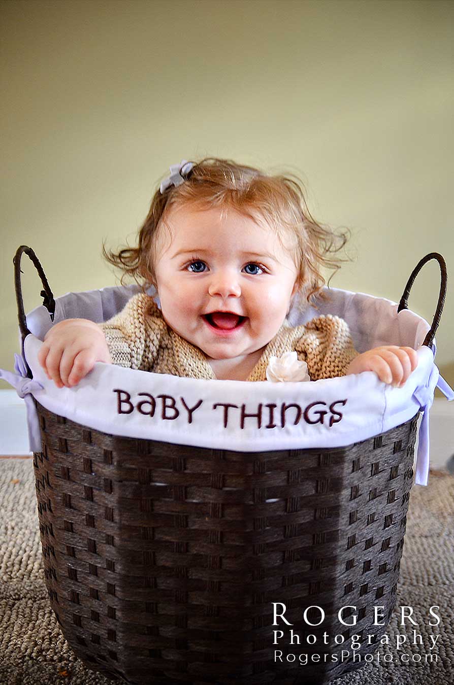 A baby is sitting in a basket that says baby things for a portrait by Rogers Photography.