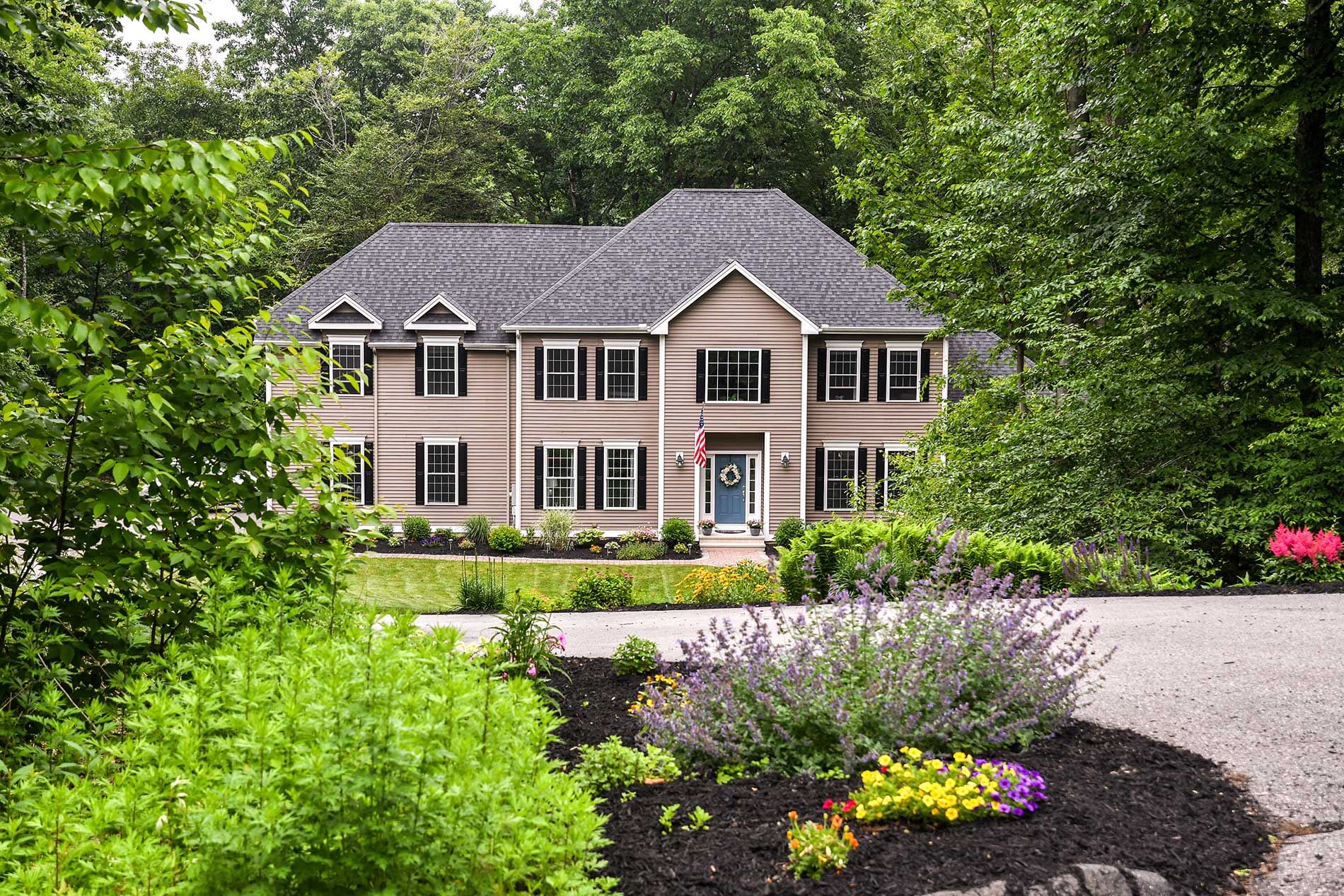 A large house is surrounded by trees and flowers for Real Estate photography by Rogers Photography.