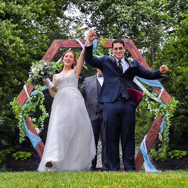 A bride and groom are holding hands in front of a wooden arch at Woodwinds wedding photography by Connecticut Wedding Photographers Rogers Photography.