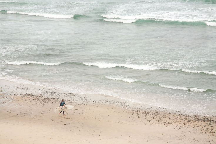 A person is standing on a beach holding a surfboard.