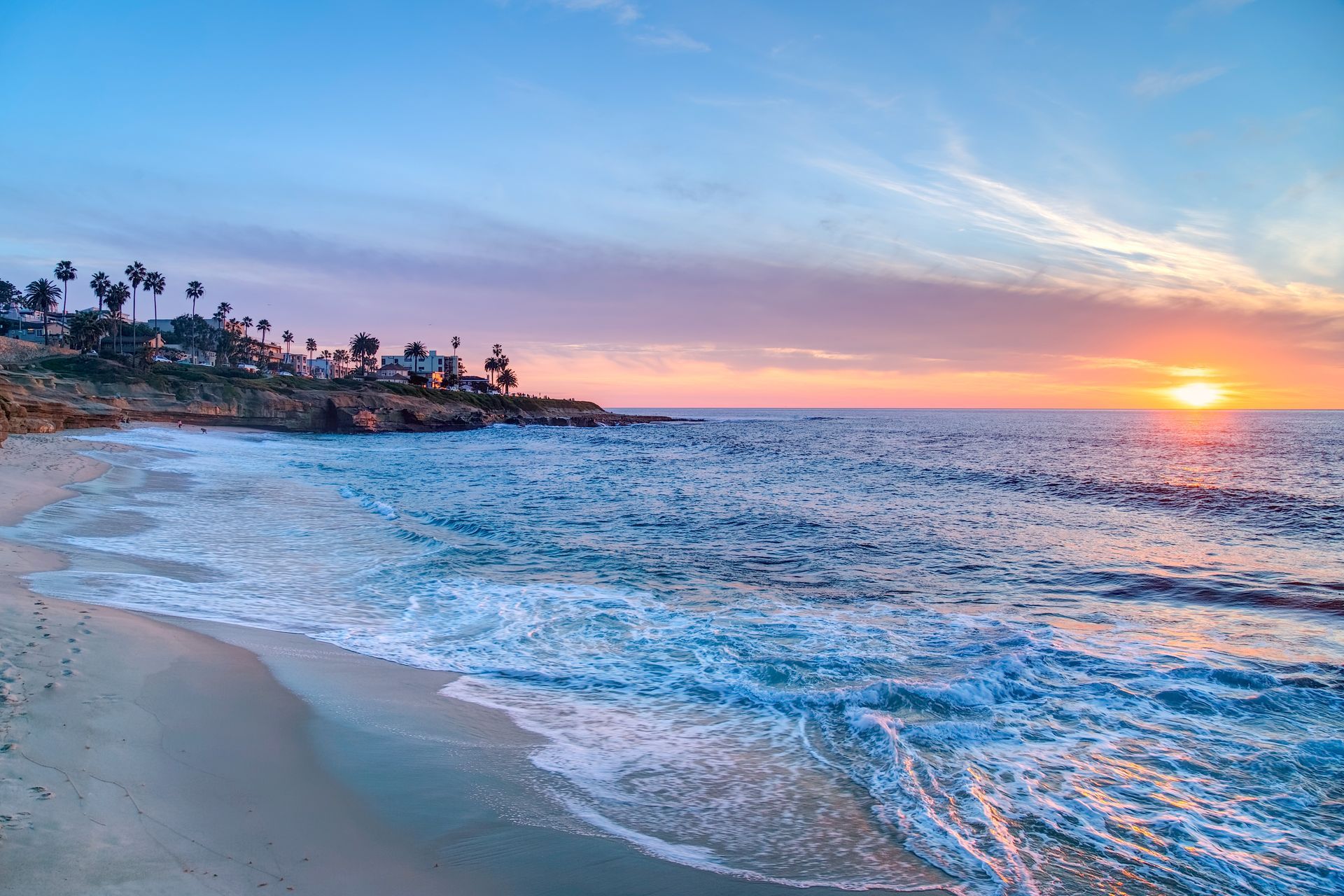 The sun is setting over the ocean and a beach with palm trees in the background.