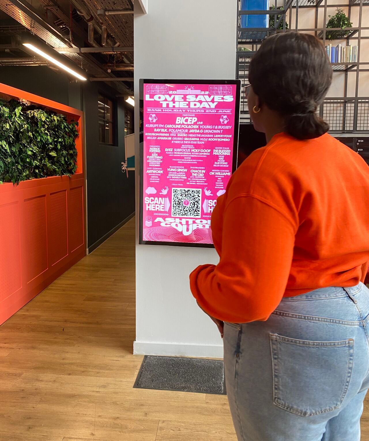 a woman in an orange sweater is standing in front of a screen that showcases an event