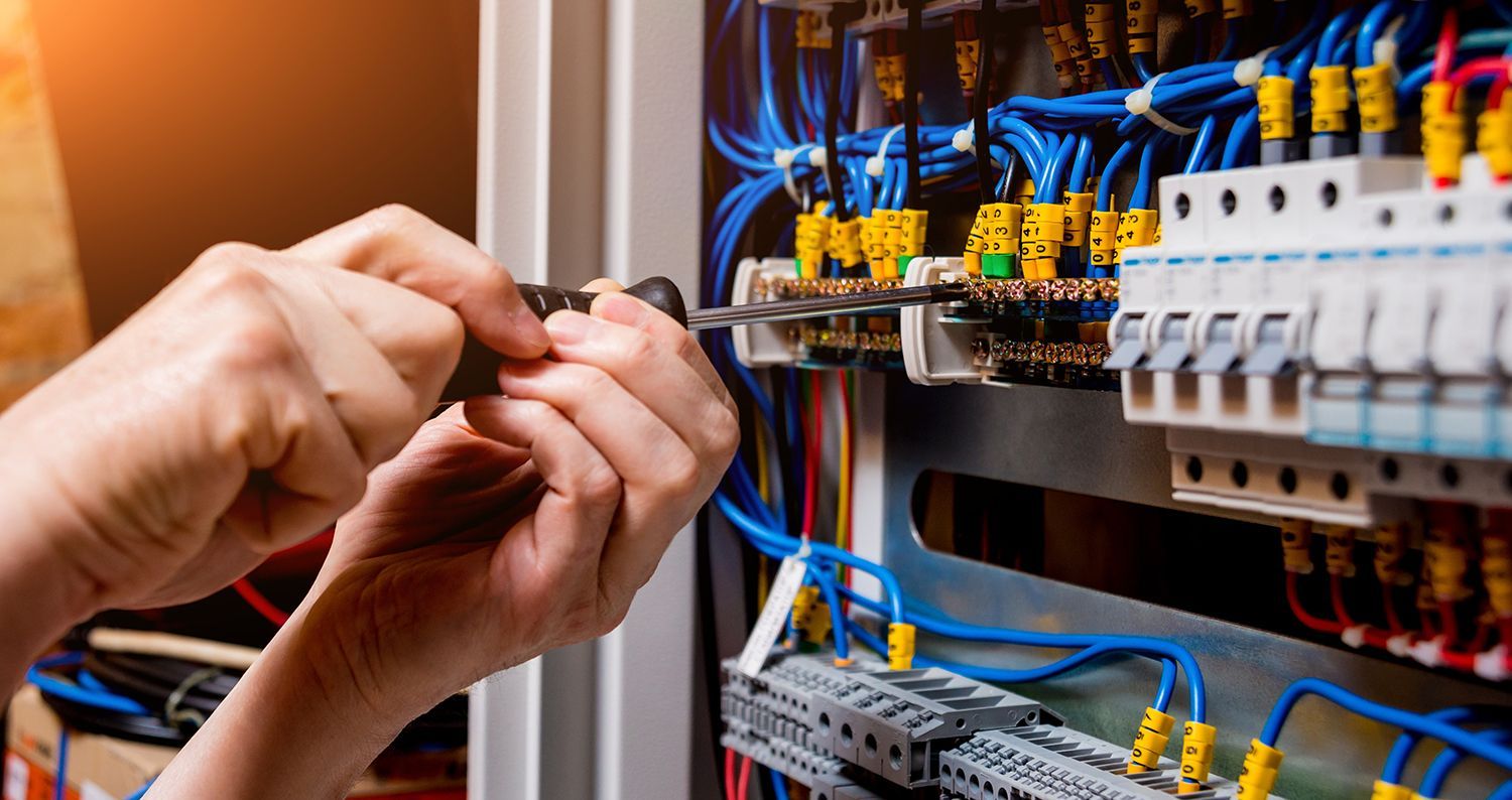 Hands wiring an electrical control panel with blue and yellow cables and circuit breakers