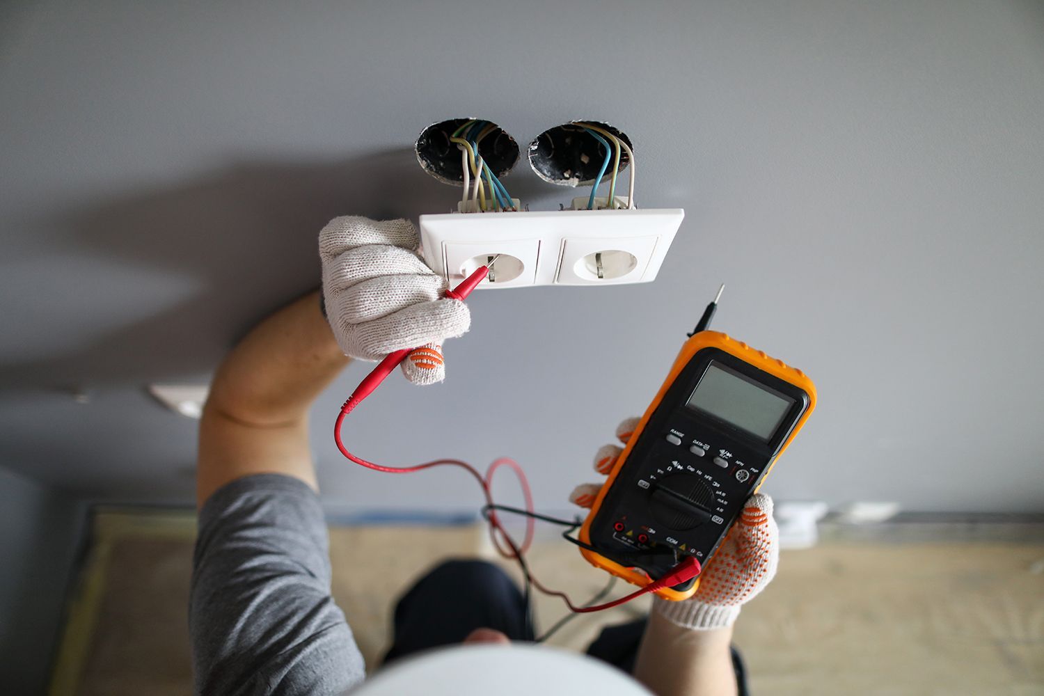 Electrician testing a ceiling light fixture with a multimeter and red wires