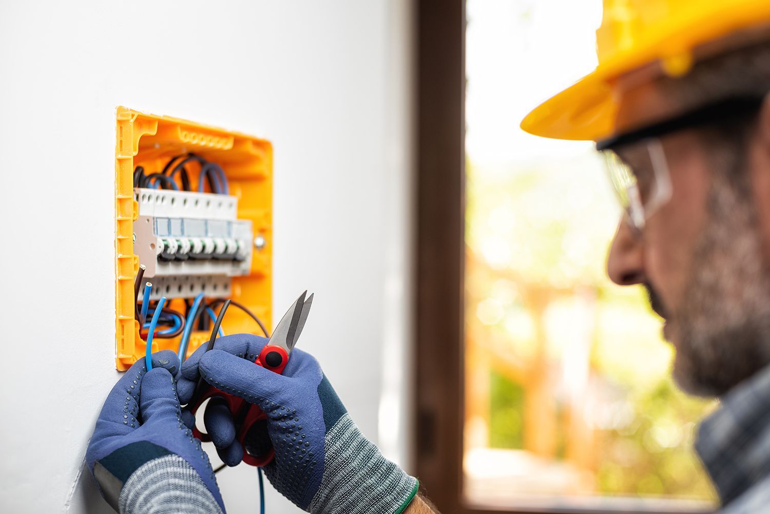 Electrician wiring an open orange circuit panel while wearing gloves and a hard hat
