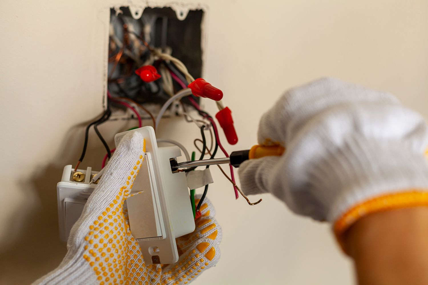 Gloved hands wiring an electrical outlet in an open wall box