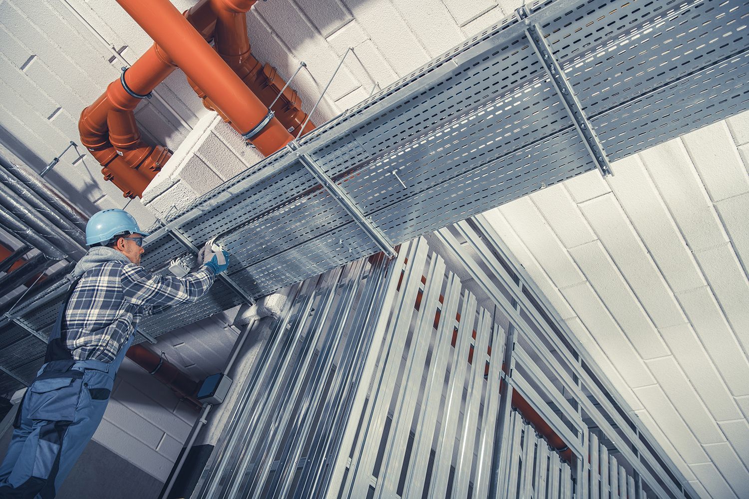 Worker on a ladder inspecting industrial pipes and metal grating in an indoor facility Worker on a ladder inspecting industrial pipes and metal grating in an indoor facility