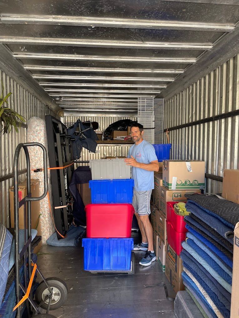 Man in a moving truck surrounded by boxes and furniture, smiling.