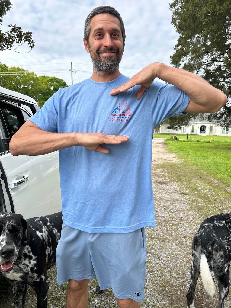 Man in blue shirt points hands toward his chest, two Great Danes stand nearby.