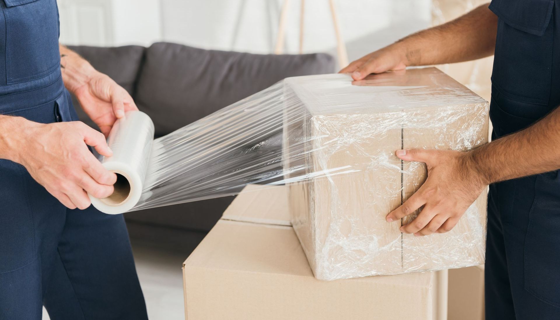 Two people wrapping a cardboard box in clear plastic wrap; moving day.