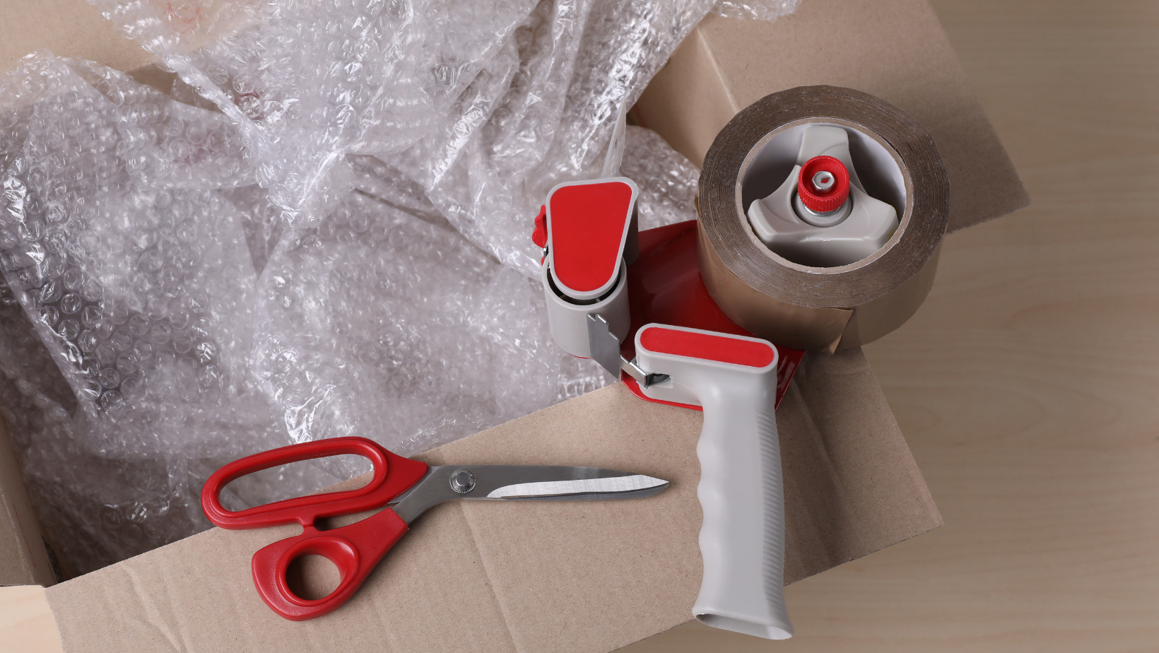 Open cardboard box with bubble wrap, packing tape dispenser, and scissors.