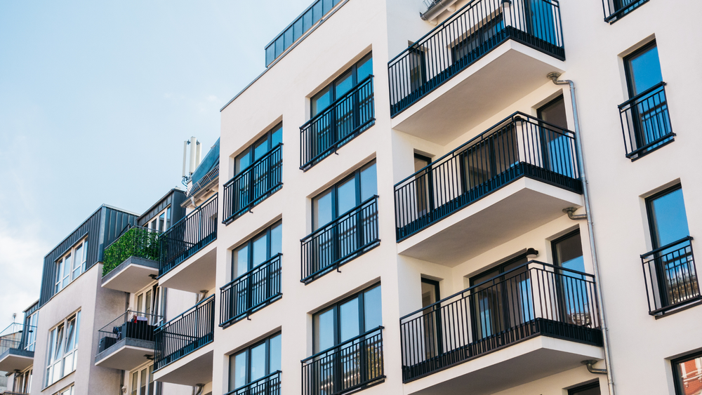 White apartment building with black balconies and window frames against a blue sky.