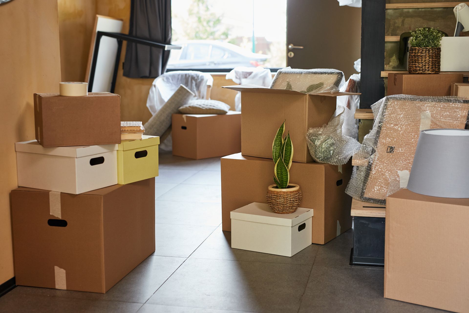 Boxes stacked in a room, indicating a move. Some items wrapped. Door visible in background.